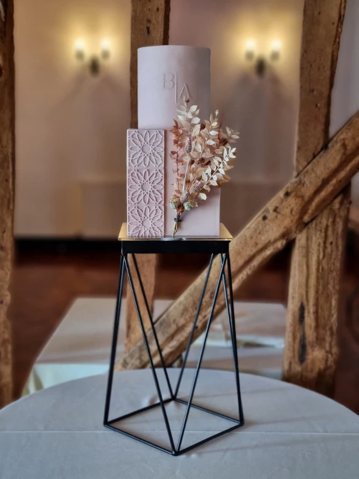 2 tier wedding cake with minimalist style monogram on top round tier and unique partial tiled effect and dried flower arrangement on bottom tier