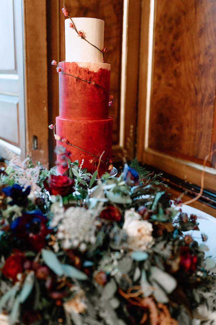 Rich dark rose red and beige textured gannache wedding cake with rice paper rose buds trailing round from bottom to top at Gosfield Hall, Essex