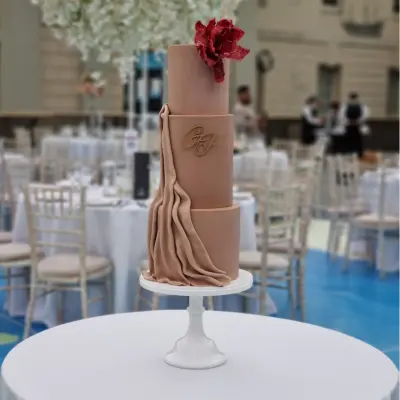 Contemporary 3 tier beige toned wedding cake with fondant drape and statement red flower National Maritime Museum London