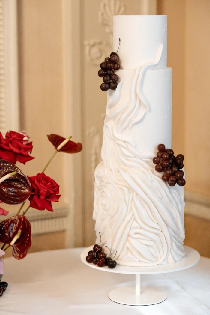 Deep red cherries and grapes styled on a contemporary textured extra tall white wedding cake at Home House, London