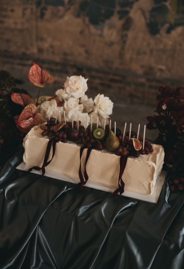 Long table wedding cake with fruit burgundy velvet ribbons and candles at Asylum Chapel, Peckham
